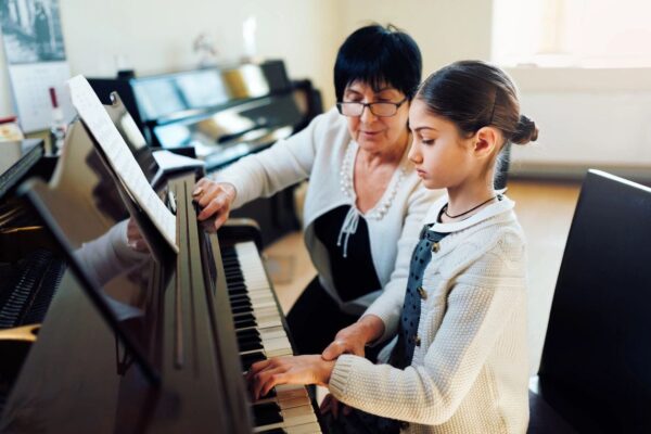 A woman and girl playing piano in front of other people.